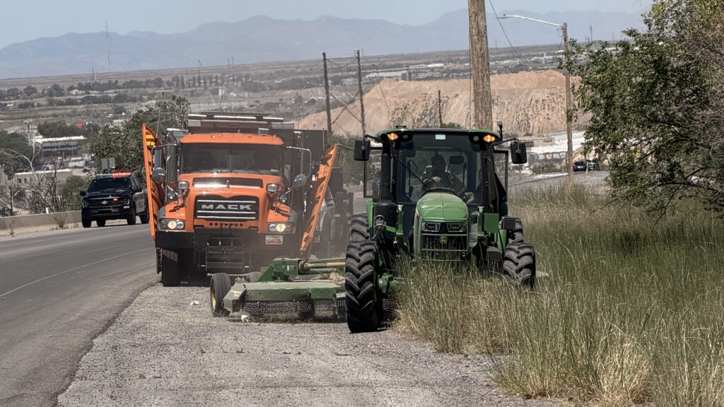 A double-wing plow follows a tractor pulling a mower through tall grass next to a road in Salt Lake City.