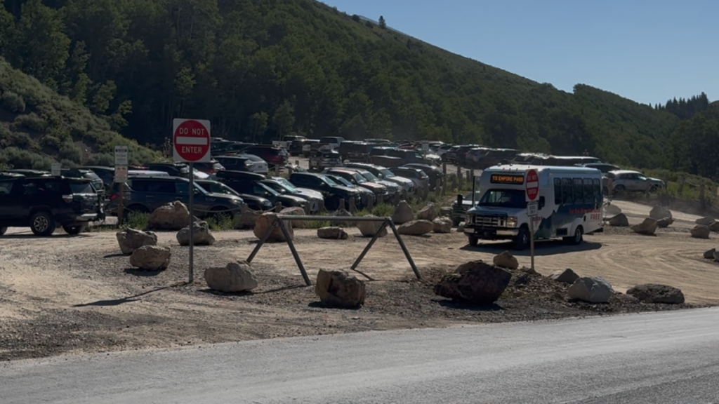 A bus stops at a dirt parking lot that is full of cars.
